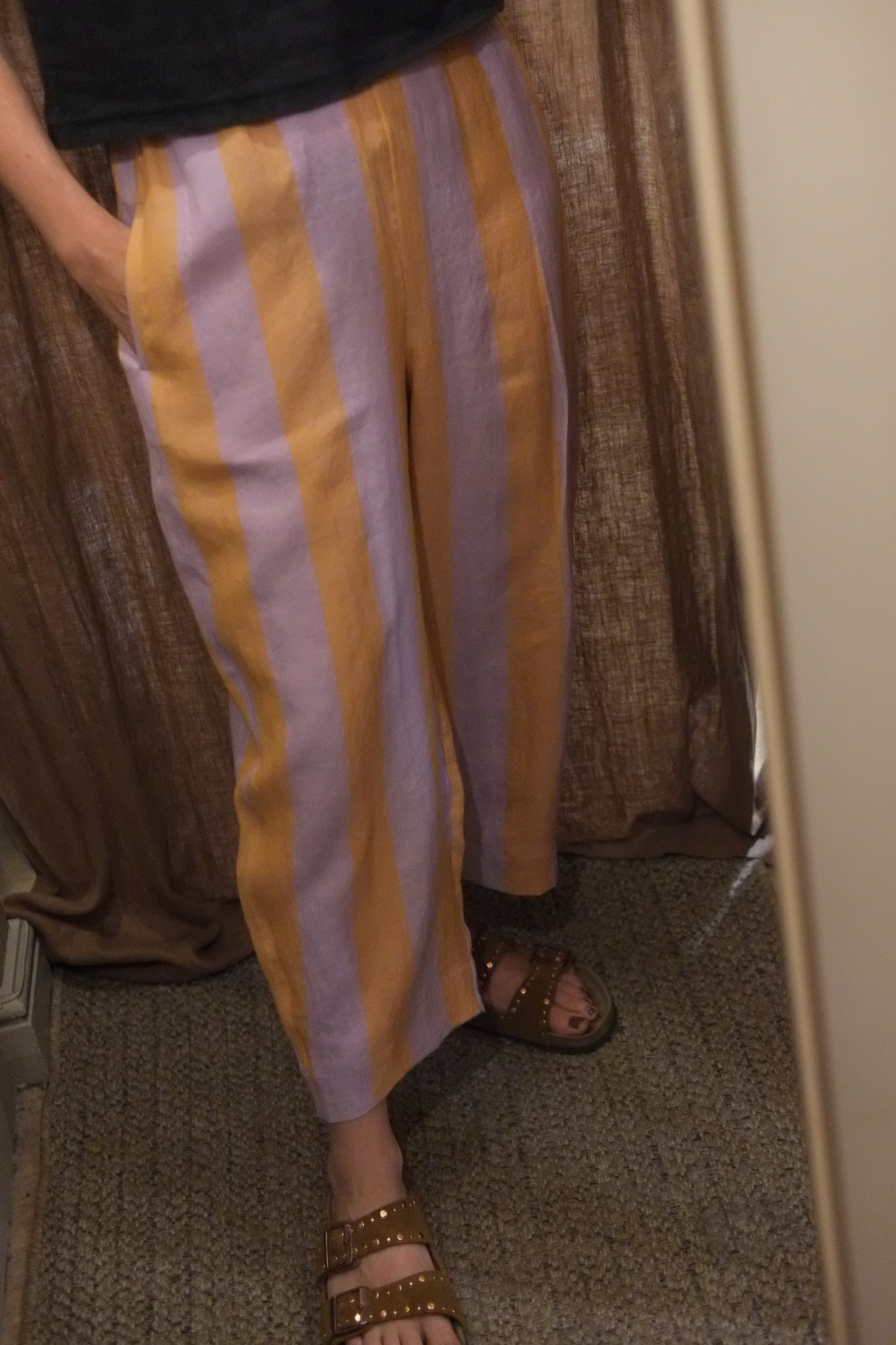 A person wearing wide-leg striped pants with alternating yellow and light lavender-purple stripes, paired with brown studded sandals, shown in a mirror selfie.