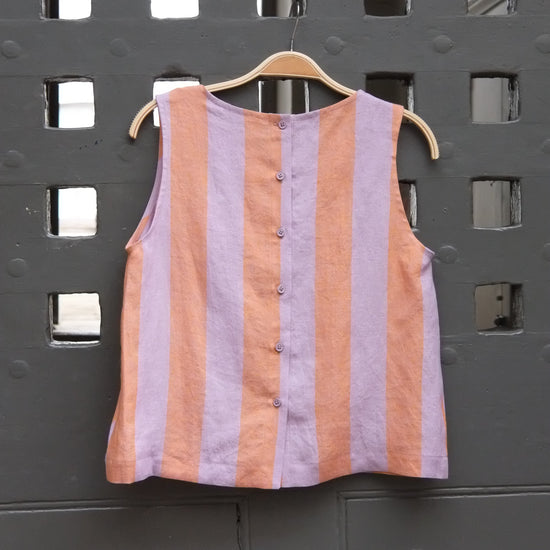 A sleeveless top with horizontal peach and lavender stripes, hanging on a dark door 