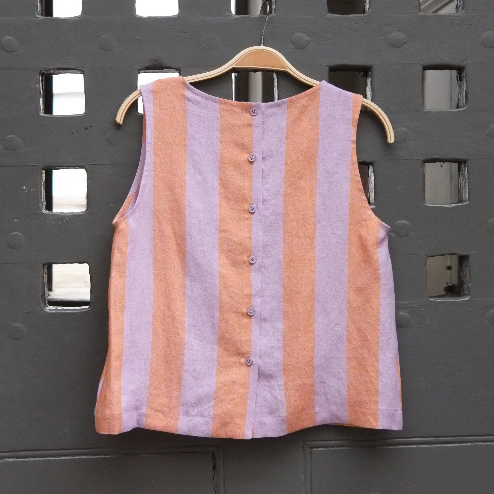 A sleeveless top with horizontal peach and lavender stripes, hanging on a dark door 