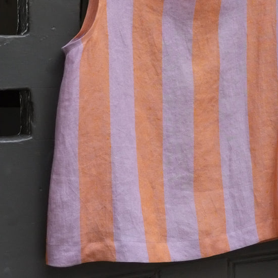 Close up of sleeveless top with horizontal lavender and orange stripes, against a dark textured background.