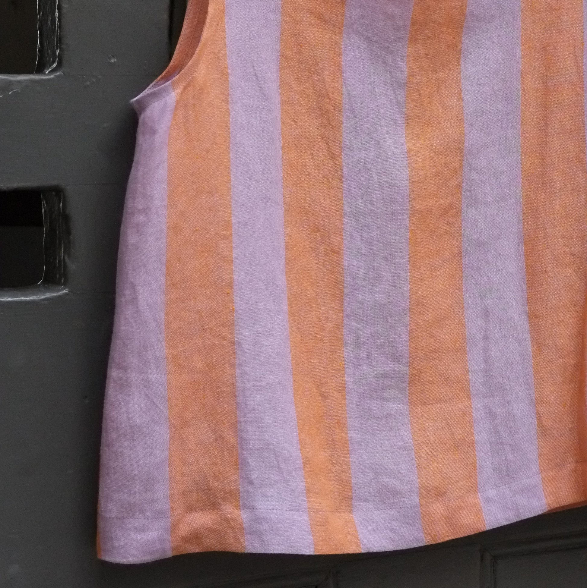 Close up of sleeveless top with horizontal lavender and orange stripes, against a dark textured background.