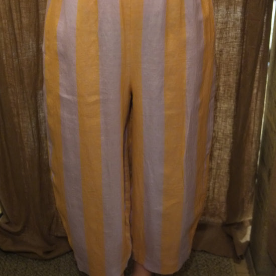 Yellow and white striped pants with a gathered elastic waistband, shown on a model wearing brown studded sandals.