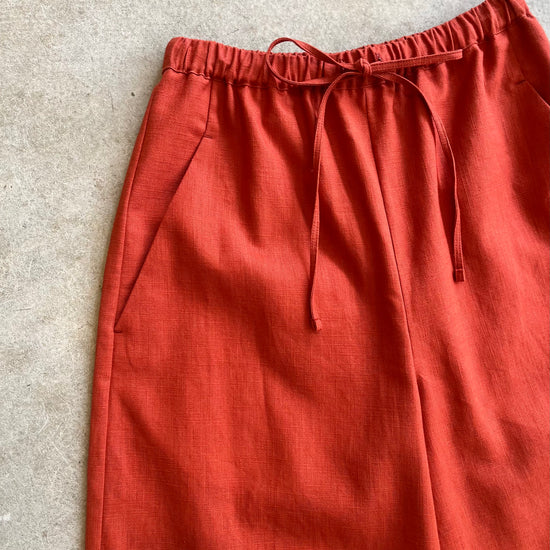 Reddish-brown drawstring linen trousers with drawstring on a light gray background