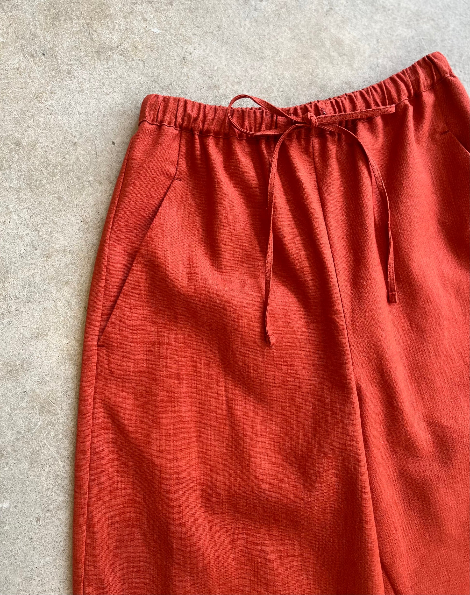 Reddish-brown drawstring linen trousers with drawstring on a light gray background