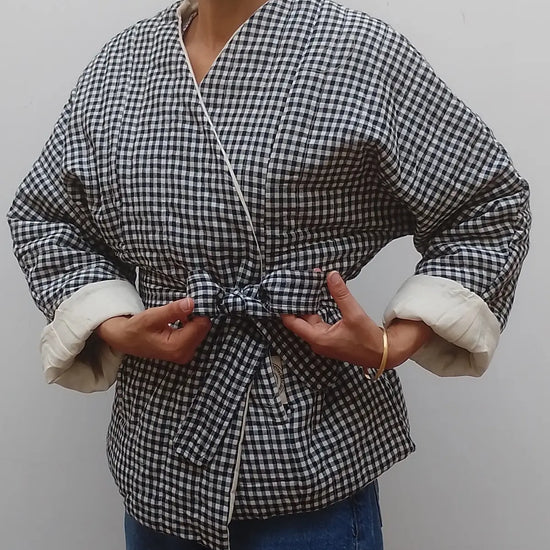 Wrap around quilted black and white gingham v neck jacket coat on model  with blue jeans on a grey background