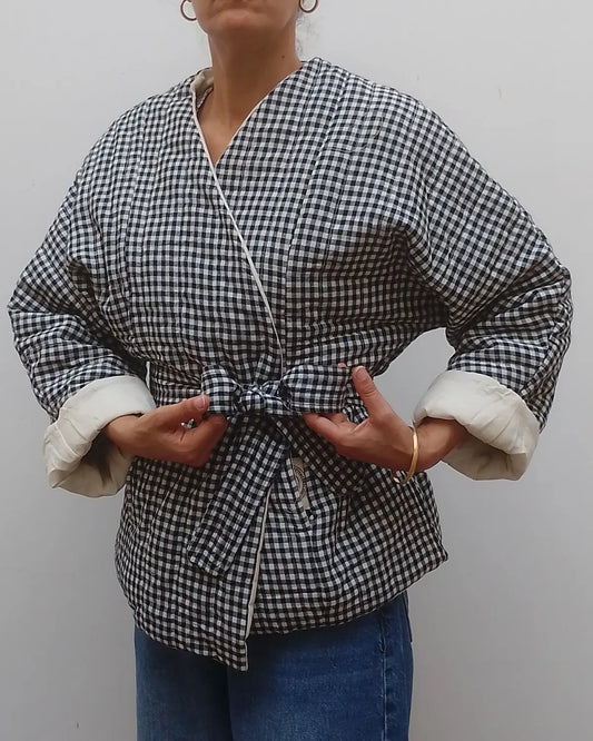 Wrap around quilted black and white gingham v neck jacket coat on model  with blue jeans on a grey background