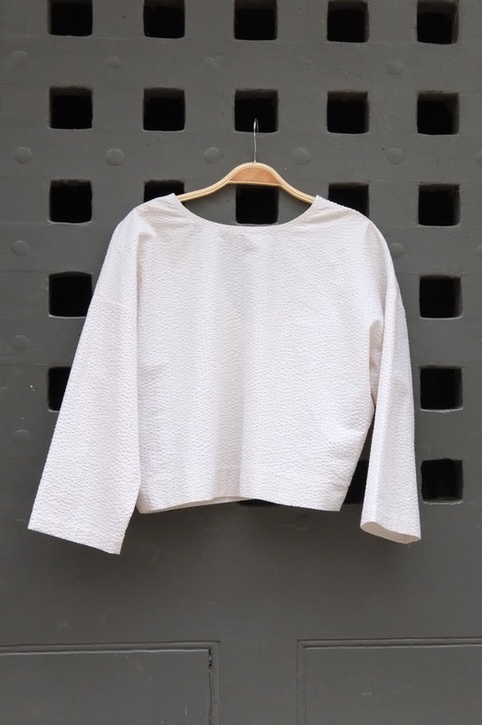 reversible top with 3/4 sleeves in cream seersucker fabric on a grey door background