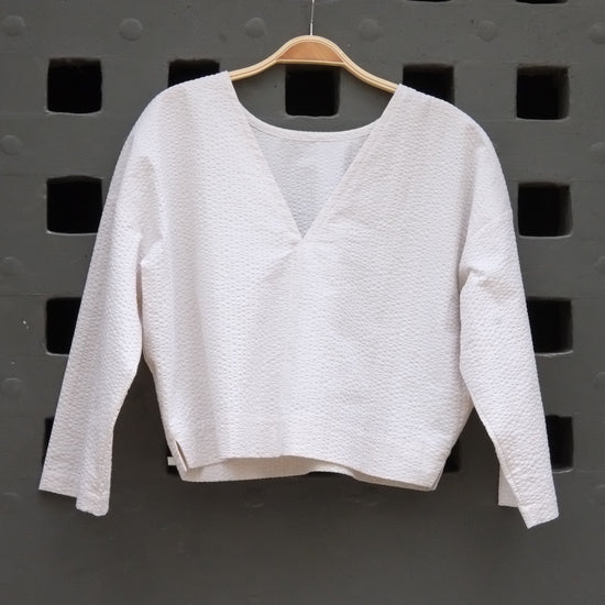reversible top with 3/4 sleeves in cream seersucker fabric on a grey door background