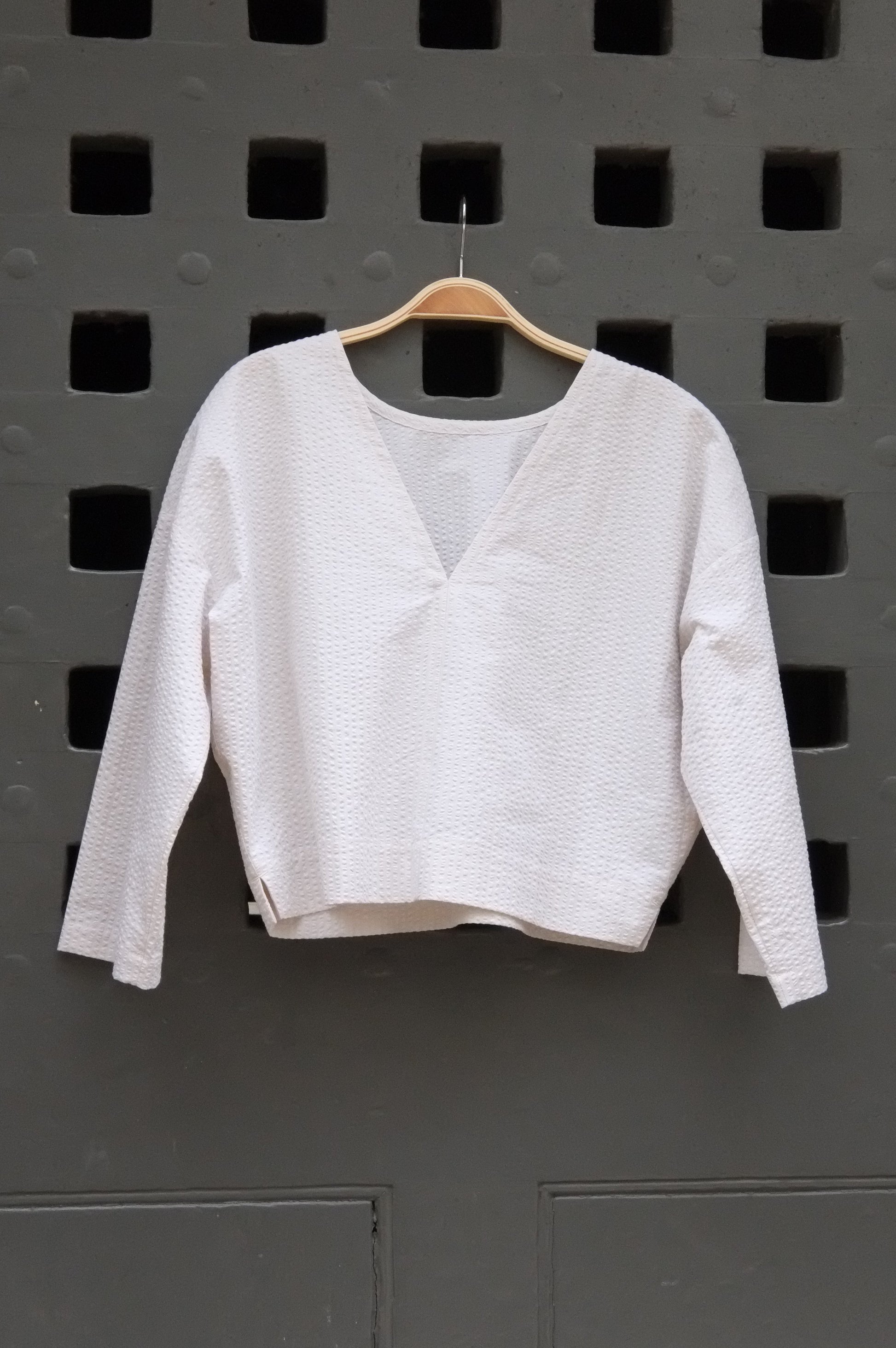 reversible top with 3/4 sleeves in cream seersucker fabric on a grey door background