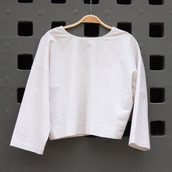 reversible top with 3/4 sleeves in cream seersucker fabric on a grey door background