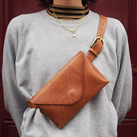 Person wearing a brown leather crossbody bag over a gray sweatshirt against a red background
