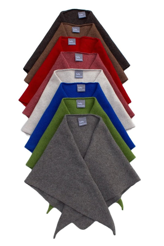 A stack of six folded knit poncho-style scarves in different colors, arranged vertically on a plain white background. The colors visible from top to bottom are dark brown, red, off-white, royal blue, olive green, and heather gray.