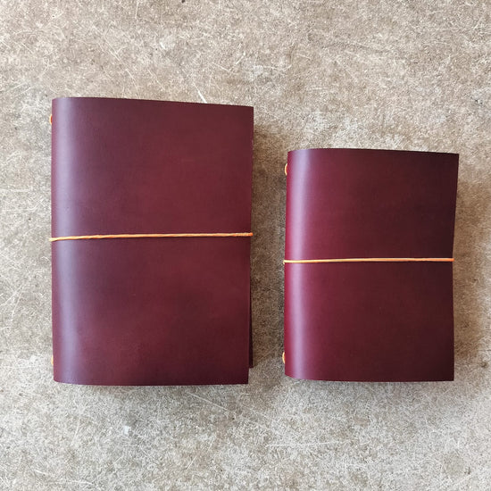 Two maroon leather-bound books with gold binding on a textured surface