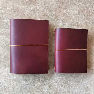 Two maroon leather-bound books with gold binding on a textured surface