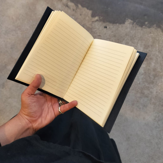 Hand holding an open notebook with lined pages on a concrete surface