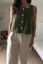 Load image into Gallery viewer, Person wearing a green sleeveless top with buttons and white pants in a room.
