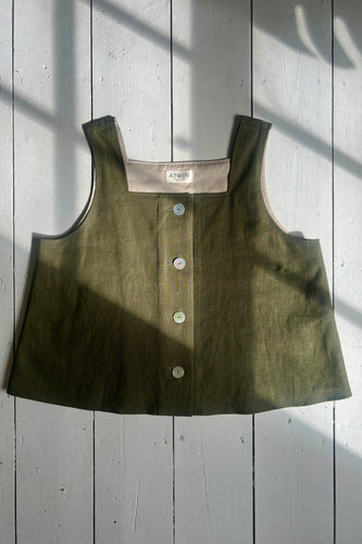 A khaki green ramie linen tank top with a square neckline, thick straps, and button-down front on a wooden background.
