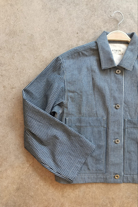 Blue and white striped workwear jacket on a hanger against a beige background