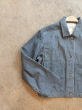 Load image into Gallery viewer, Blue and white striped workwear jacket on a hanger against a beige background
