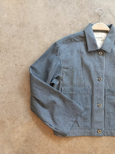 Blue and white striped workwear jacket on a hanger against a beige background