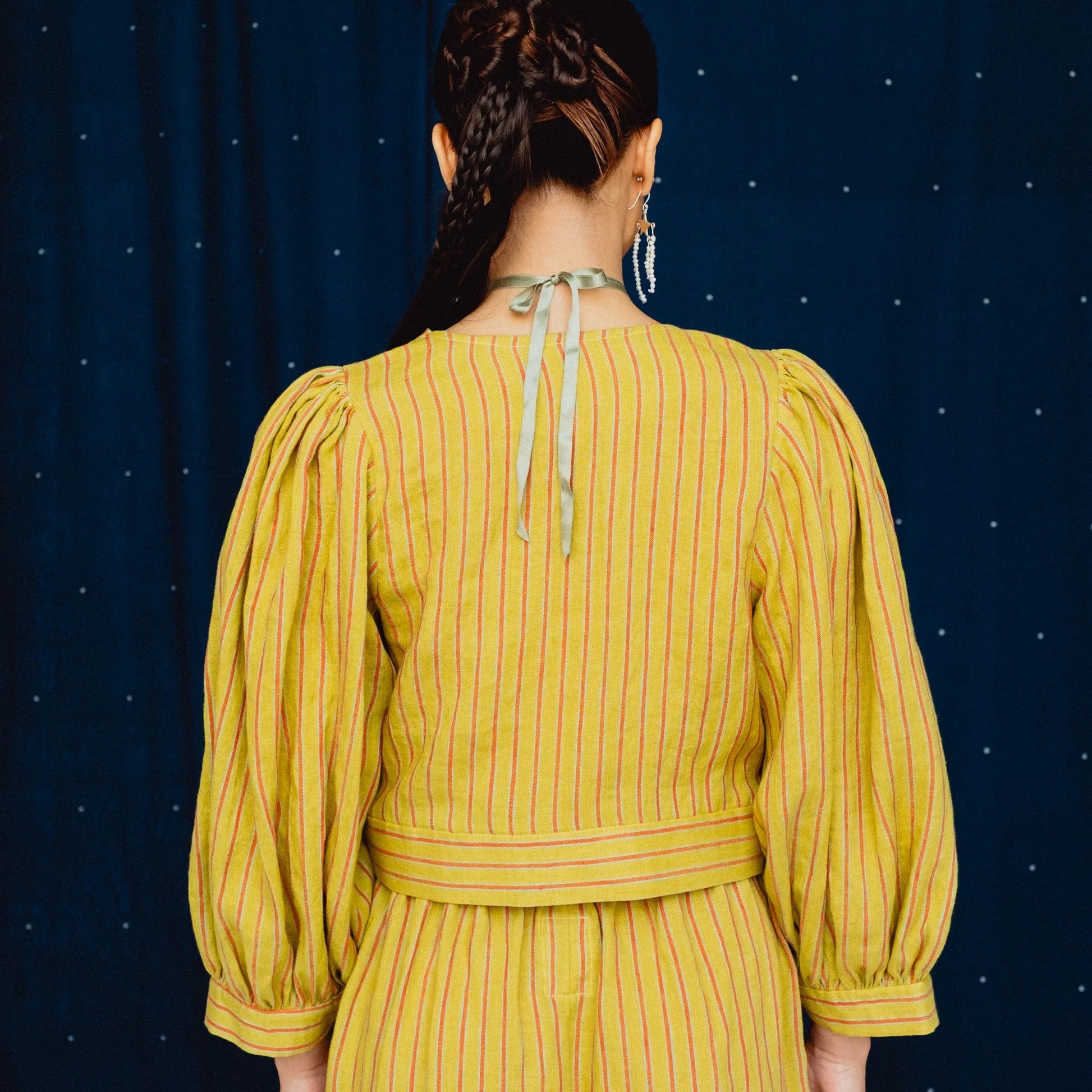 woman wearing a striped lime green wrap top on a navy blue background pictured from behind