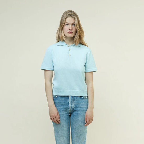 Person wearing a light blue polo shirt and jeans on a plain background
