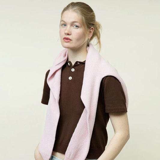 Woman wearing a brown shirt and light blue jeans with a pink vest against a plain background