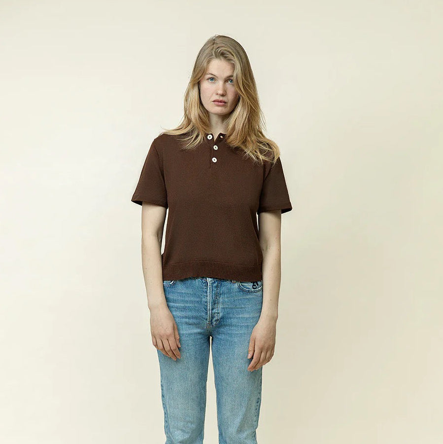 Person wearing a brown polo shirt and blue jeans on a beige background