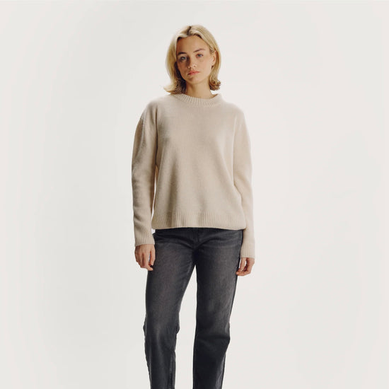 Model wearing a beige sweater and dark jeans on a plain background