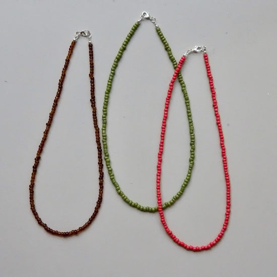 Three beaded necklaces in brown, green, and red on a gray background