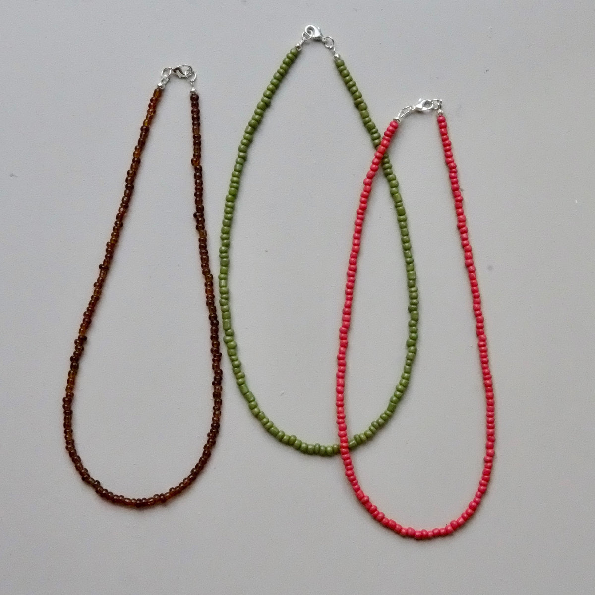 Three beaded necklaces in brown, green, and red on a gray background