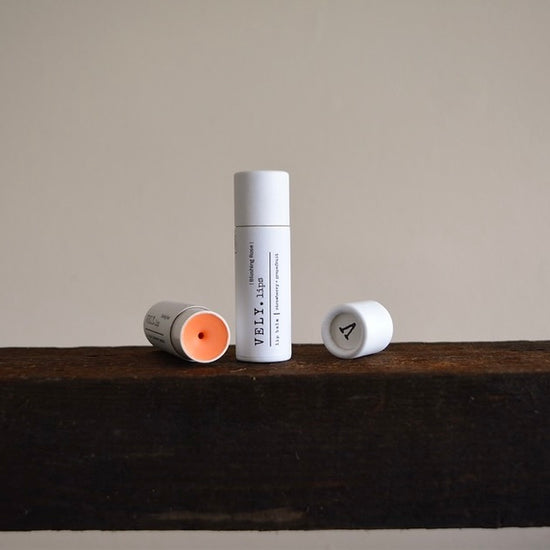 Two lip balm tubes on a wooden surface with a neutral background