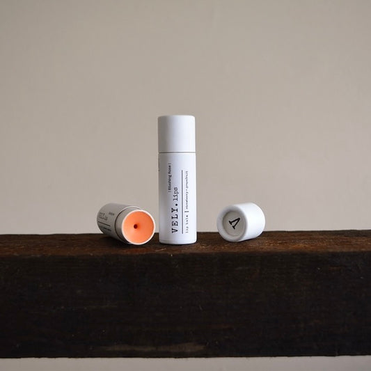 Two lip balm tubes on a wooden surface with a neutral background