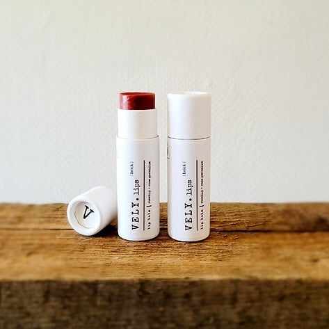Two VELV lip products on a wooden surface with a plain background