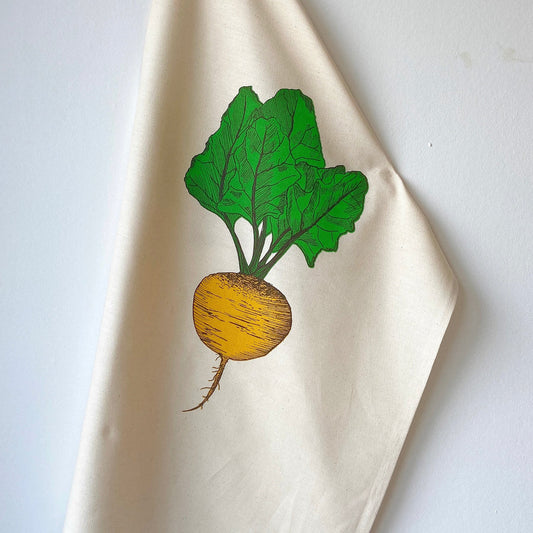 A beige cotton tea towel with a screen printed design of a beetroot with green leaves on top.