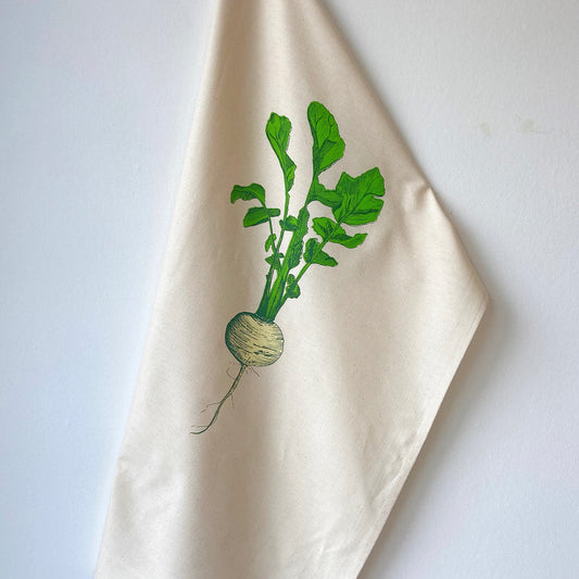 A beige cotton tea towel with a printed design of a single turnip with green leaves.