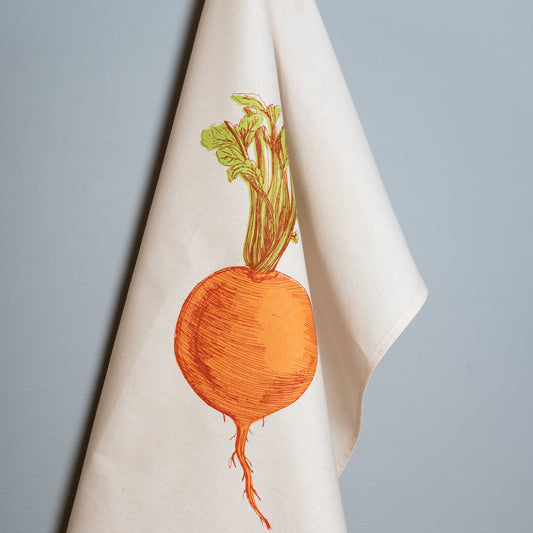 A white tea towel with an orange swede illustration printed on it, hanging on a blue background.