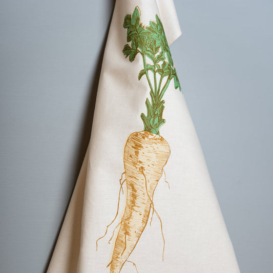 A white cotton tea towel with a printed design of a parsnip and leaves, featuring green accents on the leaves.