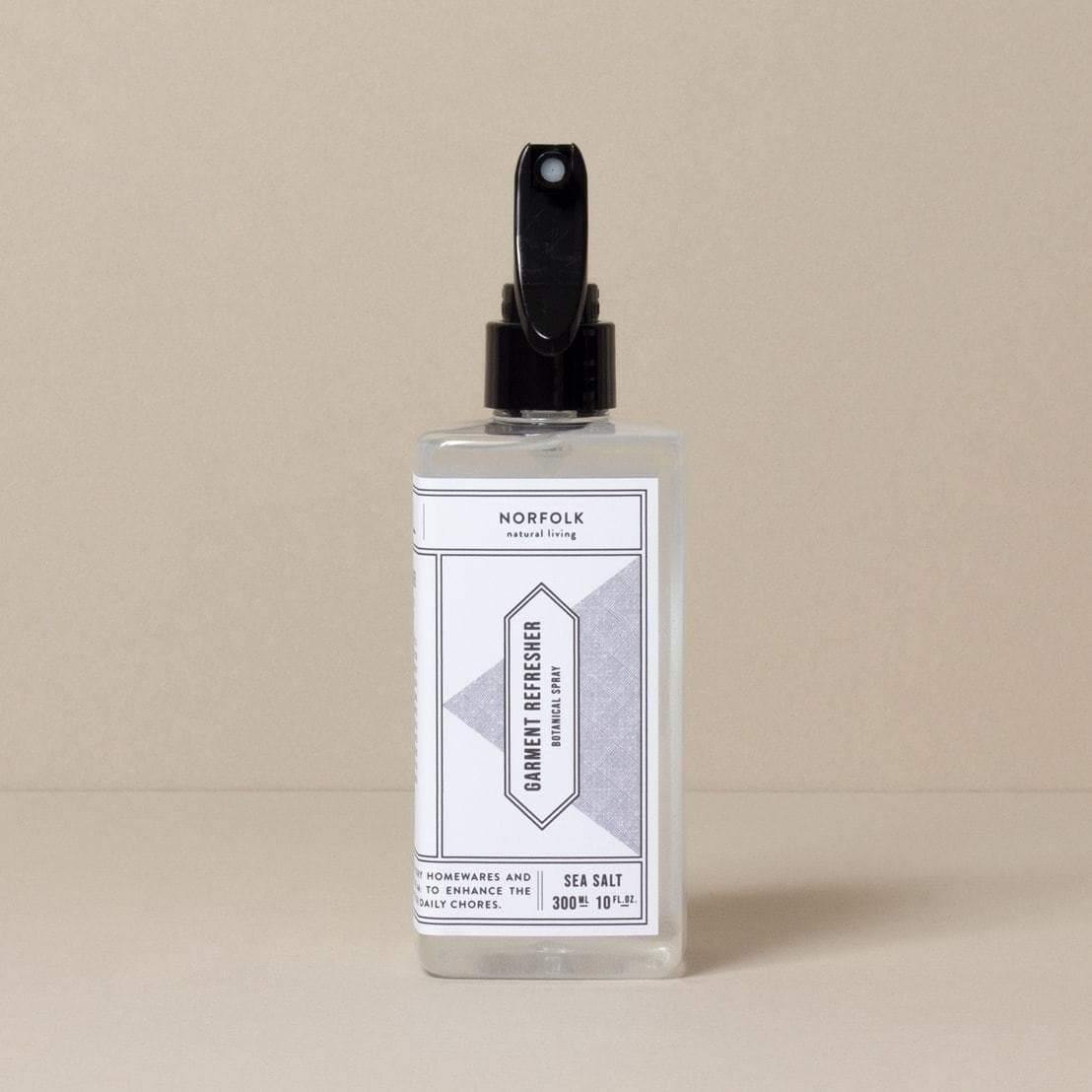  A clear bottle with a black spray pump labeled 'Garment Refresher' by Norfolk Natural Living, with Coastal Walks scent mentioned on the label.
