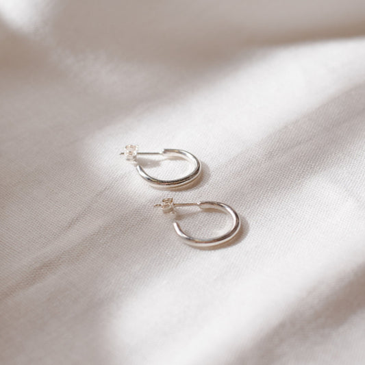 A pair of small silver hoop earrings resting on a textured fabric surface.