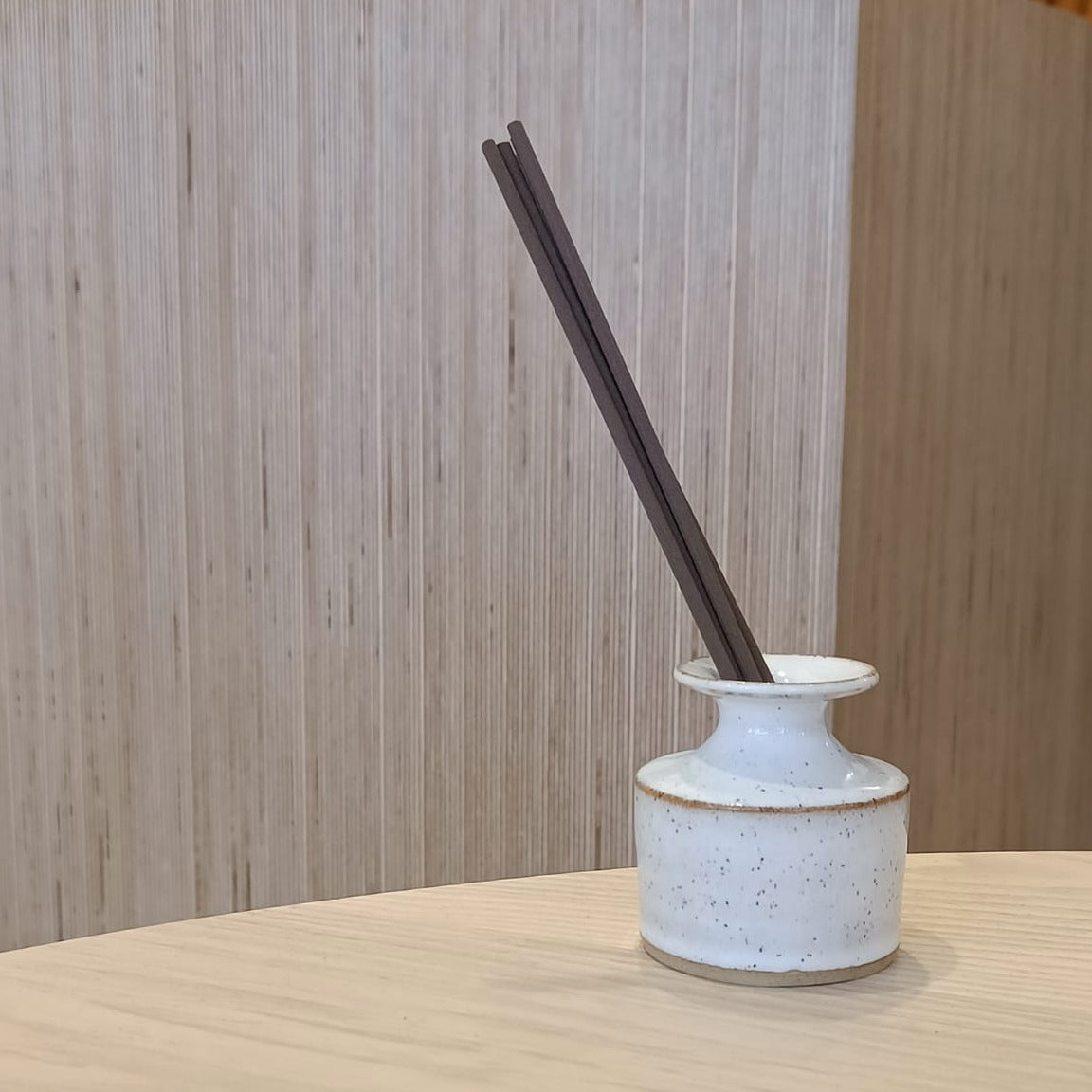 Ceramic diffuser with dark sticks on a wooden surface