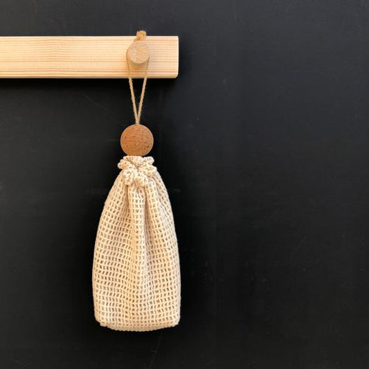 A beige cotton mesh soap bag with a drawstring and a cork ball.