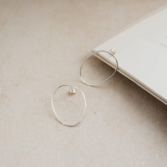 A pair of silver oval stud earrings placed on an open book.